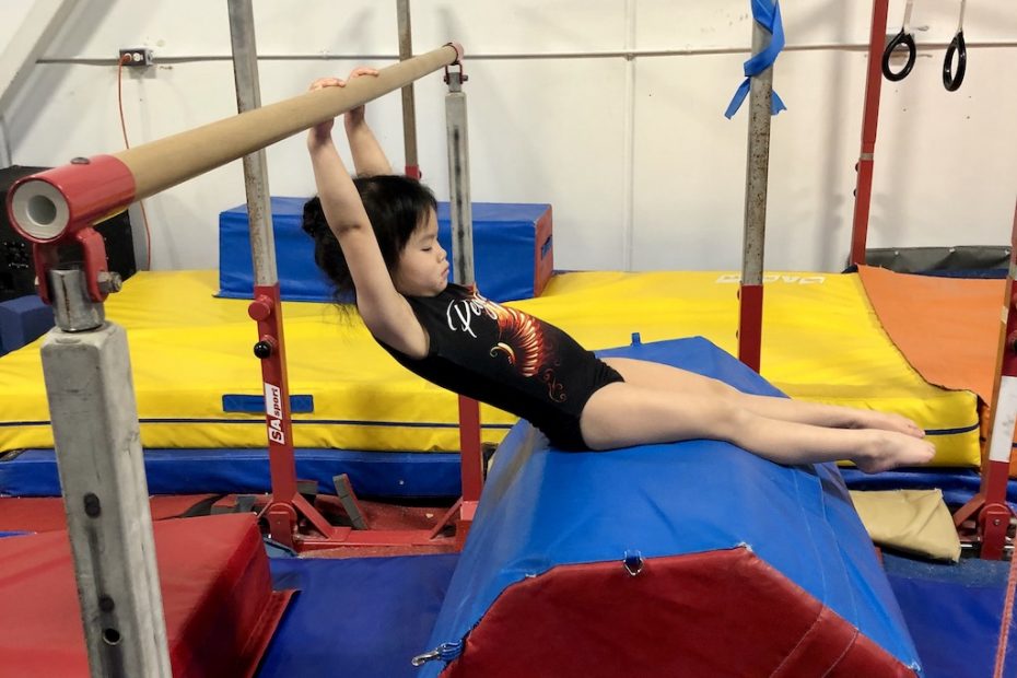 young girl hanging on bar with feet on cylinder mat