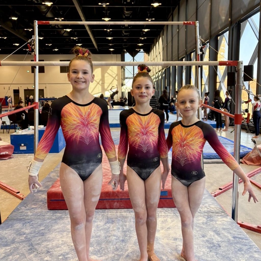 Three young athletes preparing for uneven bars at Pegasus Gymnastics.
